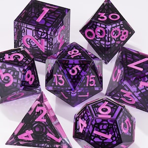 May include: A set of seven polyhedral dice featuring a translucent purple resin exterior with an intricate black internal cage structure and bright pink numbers. The collection includes a d20, d12, d10, d8, d6, d4, and a percentile die for gaming.