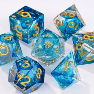 May include: A set of seven polyhedral dice made of translucent blue resin with swirling patterns, embedded glitter, and gold-colored numbers. The collection includes a d20, d12, d10, d8, d6, d4, and a percentile die, all featuring sharp edges.