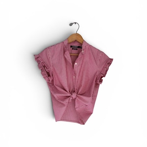 May include: A short-sleeved button-down shirt in a red and white vertical stripe pattern. The shirt features a collar, ruffled sleeve edges, and a knotted front hem. The label inside the collar reads LAUREN. The shirt is displayed on a wooden hanger.