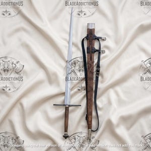 May include: A long, straight-bladed sword with a dark wooden handle and a simple crossguard. Beside it lies a matching wooden scabbard featuring intricate carved patterns, a silver-toned metal tip, and black leather straps with metal buckles.