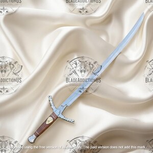 May include: A silver-colored metal sword with a curved blade and a brown wooden handle. The hilt features a metallic crossguard and a pommel, with a small decorative emblem embedded in the center of the grip. The blade is polished and reflective.