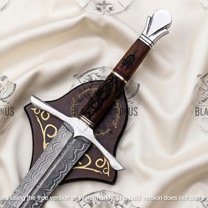 May include: A decorative sword featuring a patterned Damascus steel blade, a dark brown wooden handle with black etched detailing, and a polished silver-toned pommel and crossguard. The sword rests upon a dark brown wooden display plaque.