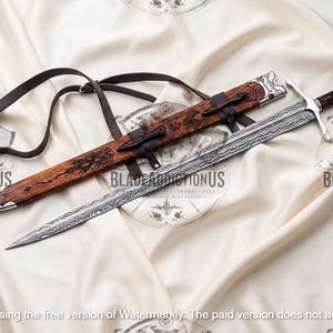 May include: A double-edged sword with a patterned Damascus steel blade, a silver crossguard, and a dark wood handle. It is accompanied by a matching wooden scabbard featuring intricate carvings, silver metal accents, and a black leather strap.