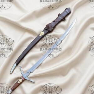 May include: A silver-toned sword with a wooden handle, a metal crossguard, and a matching brown leather scabbard featuring decorative brass accents and leather lacing. The blade is straight and polished, while the scabbard includes a belt loop.