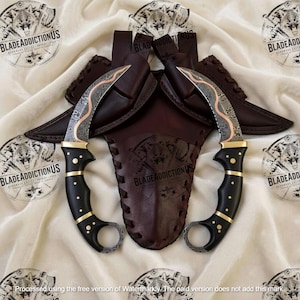 May include: Two curved karambit knives with Damascus steel blades featuring a copper spine inlay. The handles are black with brass pins and a finger ring at the base. Each knife includes a dark brown leather sheath with stitched edges.