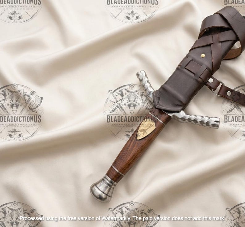May include: A dagger with a dark wood handle, a silver-toned pommel, and a twisted silver-toned crossguard. The blade is partially encased in a dark brown leather sheath featuring a strap system with metal rivets and a small gold-toned inlay.