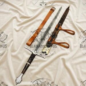 May include: A metal sword with a dark, textured handle and a silver pommel, accompanied by a wooden scabbard featuring intricate carvings and brass accents, along with a tan leather belt strap for carrying the weapon securely.