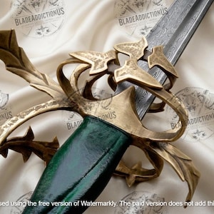 May include: A sword featuring a dark green handle and an intricate, weathered brass-toned metal hilt with leaf-like guard details. The blade displays a visible Damascus steel pattern, extending from the hilt toward the upper edge of the frame.