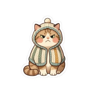 May include: A sticker featuring a brown tabby cat with a grumpy expression, wearing a cream and sage green knit hooded cape with a pom-pom on top. The cat has pink cheeks, pointed ears, and a striped tail, rendered in a flat, cartoon-style illustration.