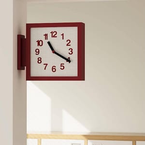 May include: A square wall-mounted clock with a deep red frame and a white face featuring a subtle grid pattern. The clock displays dark red numerals from one to twelve and has two black hands indicating the time, mounted on a side wall bracket.