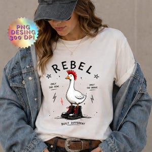 May include: A white t-shirt featuring a graphic of a white goose with a red mohawk wearing black combat boots. The text reads REBEL, ONLY THE FEW, ONLY THE BRAVE, and BUILT DIFFERENT, accompanied by small star and lightning bolt illustrations.