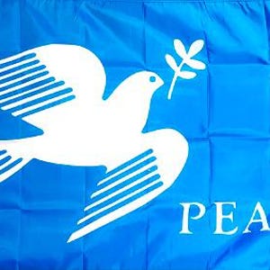 May include: A rectangular blue flag featuring a large white graphic of a dove in flight carrying an olive branch in its beak. The word PEACE is printed in white capital letters in the bottom right corner of the fabric, which has visible folds.