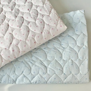 Può includere: Due pezzi di tessuto trapuntato con un motivo a cuori ripetuti. Un pezzo è bianco con contorni di cuori rosa e piccole stelle rosa, mentre l'altro è bianco con contorni di cuori azzurri e piccole stelle azzurre in tutto il design.