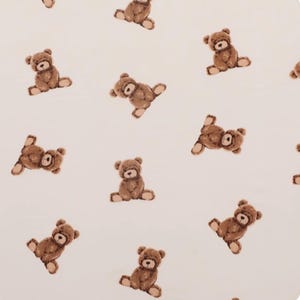 Könnte beinhalten: Ein hellcremefarbener Stoff mit einem sich wiederholenden Muster aus kleinen, braunen Teddybären. Jeder Bär ist in sitzender Position mit einer weichen, illustrierten Textur dargestellt und in verschiedenen Ausrichtungen auf der Fläche verteilt.