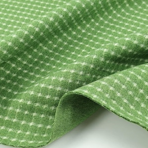 May include: A piece of green fabric featuring a small, repeating white grid pattern. The material has a soft, slightly fuzzy texture and is shown with folds that create natural shadows and highlights across the surface of the textile.