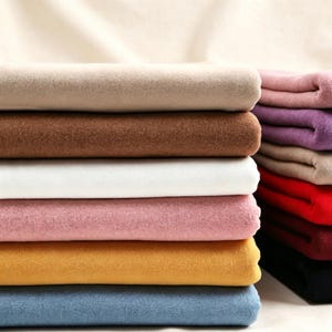 May include: A stack of folded fabric pieces in various solid colors including beige, brown, white, dusty pink, mustard yellow, and blue, with a secondary vertical stack featuring shades of pink, purple, tan, red, dark maroon, and black.