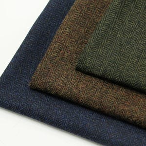May include: Three folded pieces of fabric featuring a classic herringbone weave pattern. The textile swatches are presented in distinct colours, including a deep navy blue, a rich earthy brown, and a dark forest green, each with a textured finish.