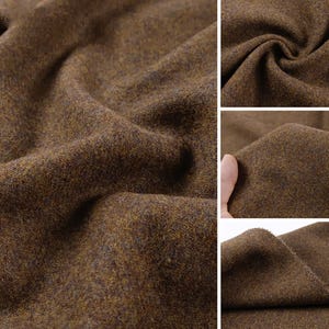 May include: A thick, textured fabric in a deep brown hue with subtle flecks of golden yellow and dark charcoal throughout. The material features a dense, felted appearance with visible fibers and soft, irregular folds across the surface.