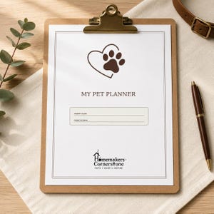 K&ouml;nnte beinhalten: Ein braunes Klemmbrett mit einem wei&szlig;en Blatt Papier, das mit MY PET PLANNER betitelt ist und eine braune Herz- und Pfotenabdruckgrafik zeigt. Die Seite enth&auml;lt Felder f&uuml;r den Namen des Besitzers, Telefon oder E-Mail und das Homemakers Cornerstone Logo.
