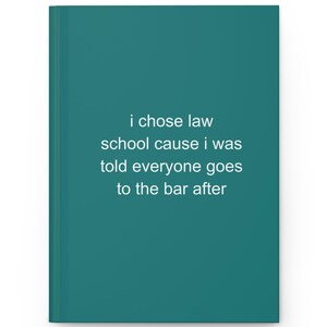 May include: A teal hardcover journal featuring the white printed text: i chose law school cause i was told everyone goes to the bar after. The notebook has a solid colored cover and a vertical spine on the left side, presenting a clean design.