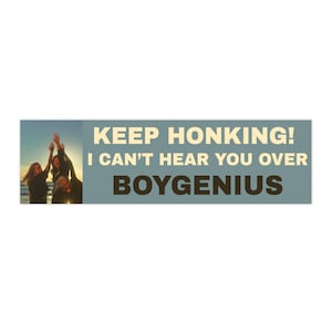 Könnte beinhalten: Ein rechteckiger Autoaufkleber mit blaugrauem Hintergrund und dem Text KEEP HONKING! I CAN'T HEAR YOU OVER BOYGENIUS in fetter cremefarbener und schwarzer Schrift, daneben ein Foto von drei Personen mit erhobenen Armen bei Sonnenuntergang.