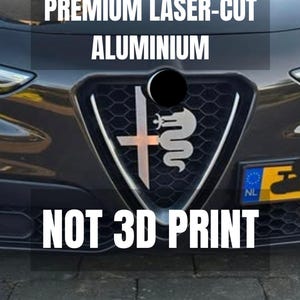 Pode incluir: Um emblema de alumínio cortado a laser prateado com uma cruz e uma serpente, montado na grade preta em formato de colmeia de um veículo. O texto PREMIUM LASER-CUT ALUMINIUM e NOT 3D PRINT está sobreposto em letras brancas maiúsculas.