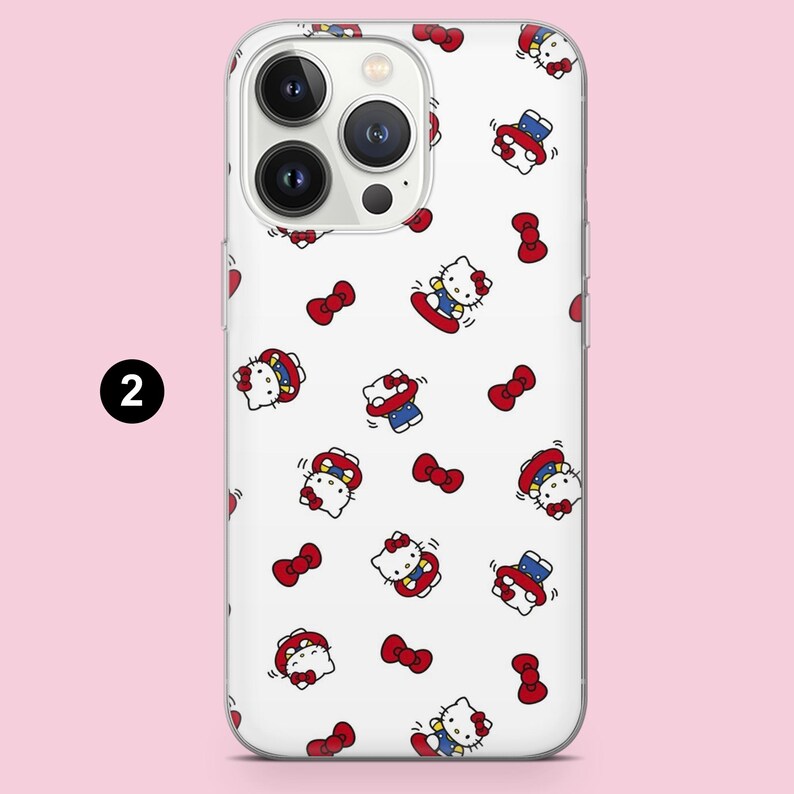 May include: A white smartphone case featuring a repeating pattern of Hello Kitty characters wearing blue outfits and red bows, interspersed with small red bows. The design is printed on a clear case, showing the phone's camera module at the top.