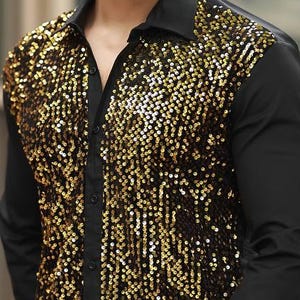 Puede incluir: Una camisa de manga larga con botones que presenta un cuello, mangas y espalda en negro sólido, con un panel frontal cubierto de lentejuelas doradas brillantes. La camisa incluye un cuello estándar, una tapeta frontal y puños.