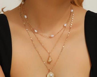 Collar minimalista de cadena dorada en capas con colgantes de perlas y conchas marinas.