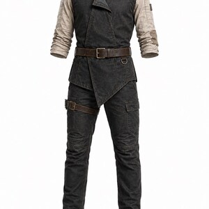 May include: A charcoal grey vest with an asymmetrical front closure worn over a beige long-sleeve shirt. The outfit includes matching charcoal grey cargo trousers with a brown leather belt and a brown leg strap, finished with dark brown boots.