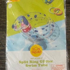 May include: A Sun Squad inflatable split ring glitter swim tube in a dog shape with blue spots and a red collar with white stars. The packaging displays the product name, a warning label, and dimensions of 23 inches by 18.5 inches by 14.5 inches.