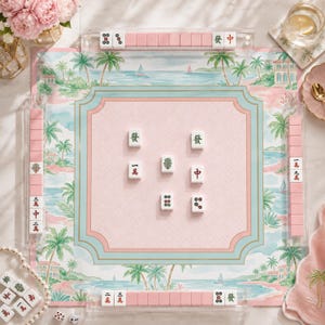 May include: A Mahjong set featuring a pink and blue tropical-themed play mat with palm trees and coastal scenery. The set includes white tiles with Chinese characters and symbols, arranged in clear acrylic racks and on the central play area.