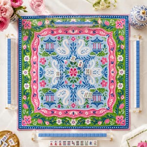 May include: A square mahjong mat featuring a light blue center with white swans, floral motifs, and blue pagodas, framed by a pink and green border. Four clear acrylic racks hold blue and white tiles, with additional tiles scattered on the mat.
