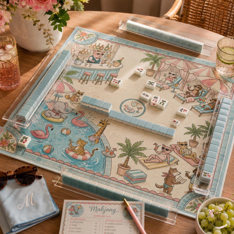 May include: A Mahjong board game set featuring a colorful illustrated play mat with a pool party theme, light blue tiles, four clear acrylic tile racks, a score card with the text Mahjong, and a pink pen, all arranged on a wooden surface.