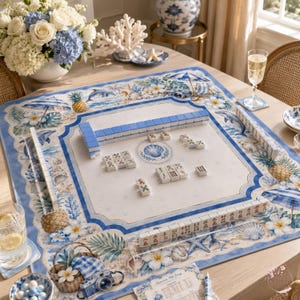 Peut inclure: Un tapis de mah-jong carr&eacute; au motif c&ocirc;tier avec des illustrations bleues et blanches de dauphins, d'ananas, de coquillages et de parasols. Le tapis comprend des supports de tuiles en acrylique transparent et des tuiles de mah-jong dispos&eacute;es.