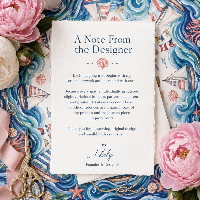 以下が含まれることがあります： A Note From The Designerというタイトルの濃い青色のテキストが印刷された、縁がギザギザの白い長方形のカード。マージャンマットの製造工程について説明されており、創設者兼デザイナーのAshelyの署名と小さなサンゴのアイコンが添えられています。