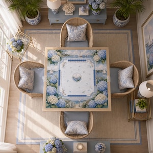 Puede incluir: Una mesa de juego cuadrada con un tablero de tem&aacute;tica costera, bordes de flores de hortensia azules, veleros y un motivo n&aacute;utico central, rodeada por cuatro sillas de rat&aacute;n trenzado con cojines azul claro y almohadones.
