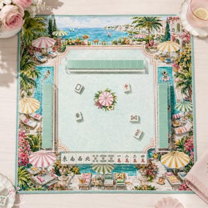 May include: A Mahjong set featuring a rectangular play mat with a coastal resort illustration, including palm trees, umbrellas, and lounge chairs. The set includes light green tiles arranged in racks and scattered on the mat, with a central floral motif.