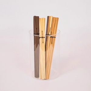 May include: A glass jar filled with a variety of wooden chopsticks. The chopsticks are brown, light brown, and natural wood color. The chopsticks are bundled together with a black string.