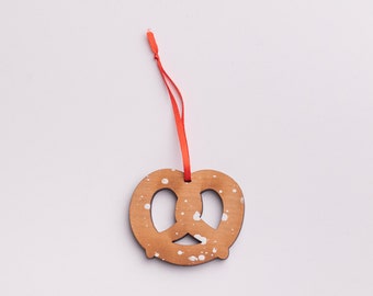 May include: A wooden pretzel ornament with white paint splatters, hanging from a red ribbon.