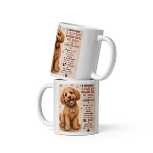 May include: Two white ceramic mugs stacked vertically, each featuring a graphic of a golden-brown cockapoo puppy wearing a tag. The text reads: A HAPPY HEART IS FILLED WITH WAGGING TAILS, WET NOSES, and ENDLESS LOVE! Be kind, Be silly, Be brave, Be grateful, Find joy in the little things, Give love freely, Choose happiness, BE YOU! Life is better with a cockapoo and a happy heart.