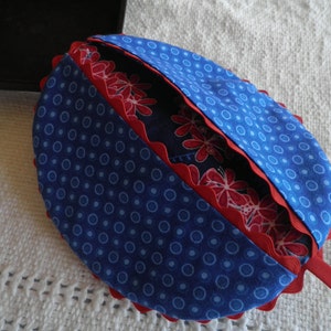 May include: A blue and red fabric pot holder with a scalloped edge and white polka dots. The pot holder is folded in half and has a red handle.