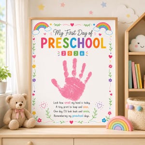 May include: A white poster in a wooden frame featuring the text My First Day of PRESCHOOL 2026, a pink handprint in the center, and a poem. The design includes colorful rainbows, hearts, and flowers, with the year 2026 displayed in square blocks.