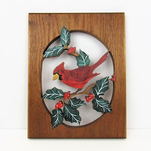 May include: A wooden wall hanging with a carved oval frame featuring a red cardinal perched on a holly branch with green leaves and red berries.