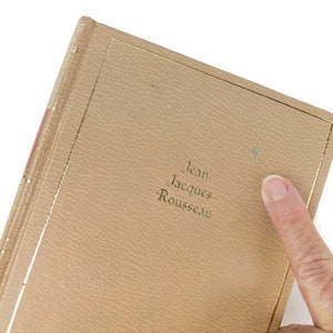 Pode incluir: Um livro encadernado em couro castanho com detalhes dourados e o texto "Jean Jacques Rousseau" na capa.