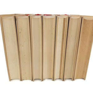 Pode incluir: Um conjunto de oito livros com capas bege e lombadas vermelhas. Os livros est&atilde;o dispostos em semic&iacute;rculo.
