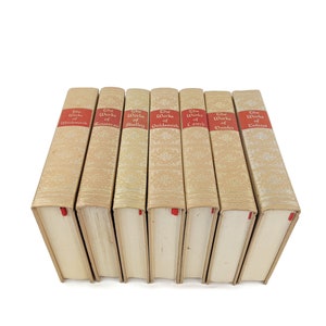 Pode incluir: Um conjunto de sete livros antigos de capa dura com lombadas douradas e etiquetas vermelhas. As etiquetas dizem "The Works of Wordsworth", "The Works of Rousseau", "The Works of Shelley", "The Works of Goldsmith", "The Works of Lamb", "The Works of Dante" e "The Works of Tolstoy".