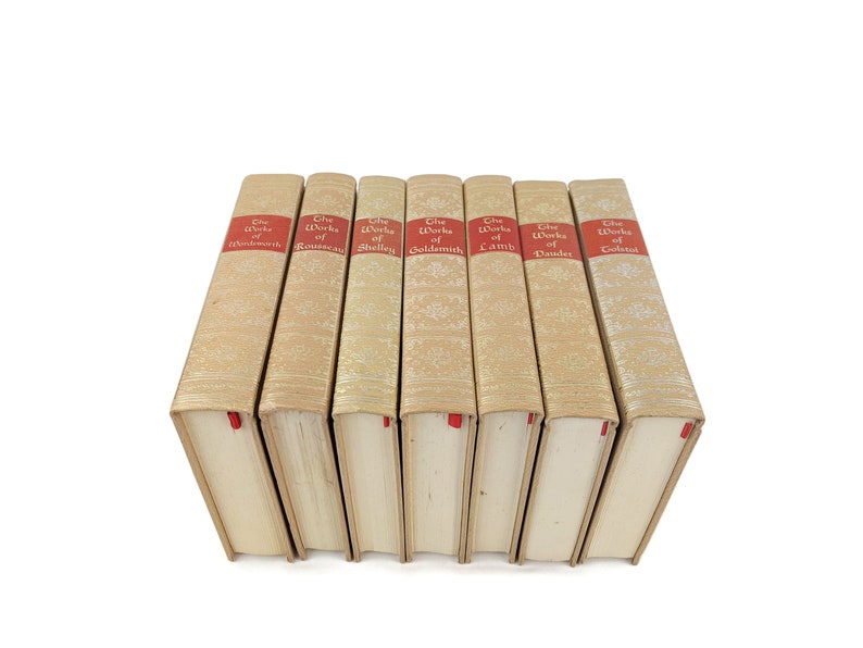 Pode incluir: Um conjunto de sete livros antigos de capa dura com lombadas douradas e etiquetas vermelhas. As etiquetas dizem "The Works of Wordsworth", "The Works of Rousseau", "The Works of Shelley", "The Works of Goldsmith", "The Works of Lamb", "The Works of Dante" e "The Works of Tolstoy".
