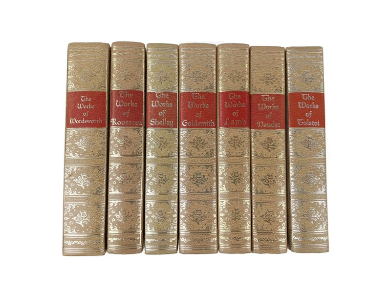 May include: A set of eight gold-colored books with red spines. The books are arranged in a row and each has a title that reads 'The Works of' followed by the author's name. The authors are Wordsworth, Rousseau, Shelley, Goldsmith, Lamb, Daudet, and Tolstoy.