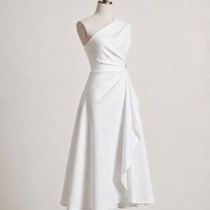 May include: A white midi-length dress featuring an asymmetrical one-shoulder neckline, a fitted bodice with diagonal pleating, and a flared skirt with a cascading side drape. The fabric has a subtle, repeating pattern of small, light-colored dots.